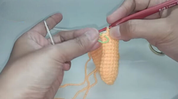 Crocheting orange amigurumi piece with green stitch marker attached