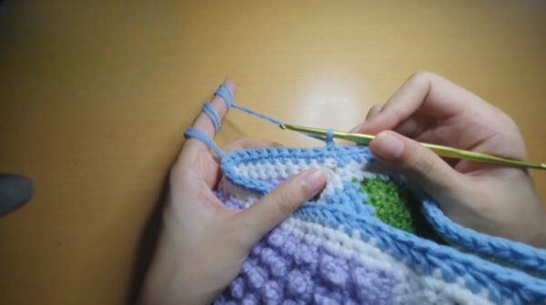 Blue yarn wrapped on fingers while flipping the work over.