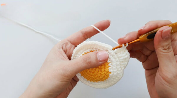 Crocheting petal stitches around daisy pouch edge