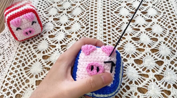 Embroidering face details on crochet dice pig