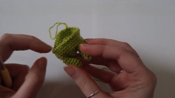 Fingers pushing stuffing into a green crocheted leg piece.
