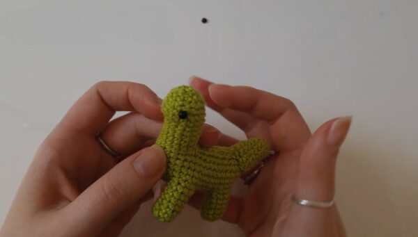 Finished green crochet dinosaur figure with a bead eye glued on.