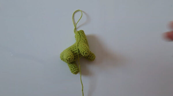 Green crochet dinosaur legs hanging with yarn tail attached.