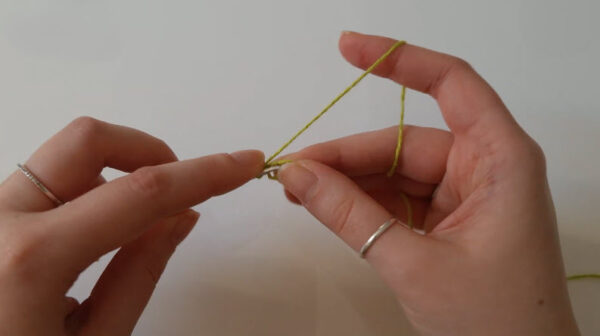 Green thread looped around fingers before starting a magic ring.
