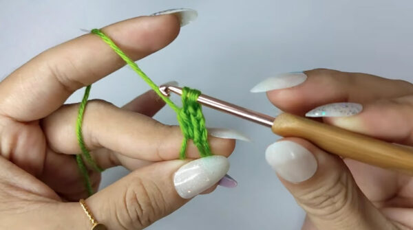 Hands crocheting a green granny stitch with gold hook.