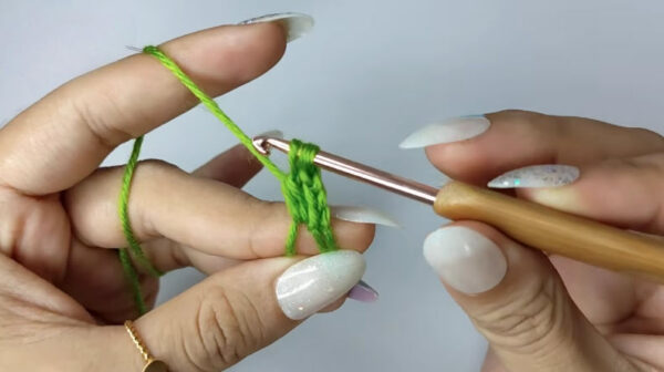 Hands crocheting a green granny stitch with gold hook.