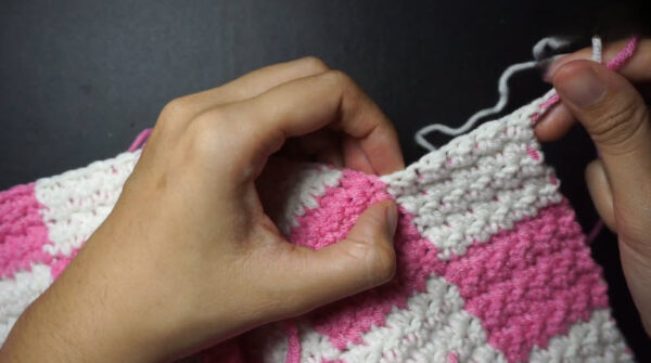 Hands holding finished pink and white checkered crochet piece.