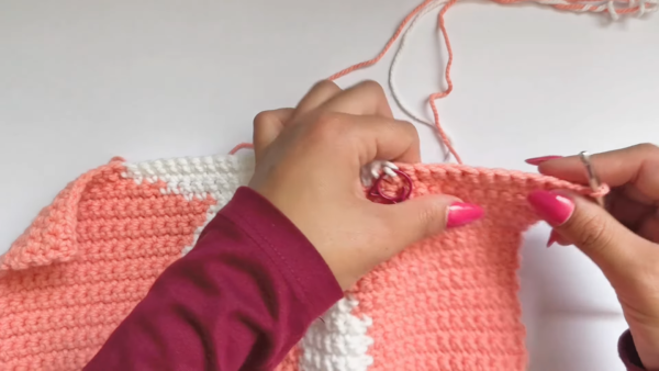 Hands joining peach and white crochet panels with stitch marker.