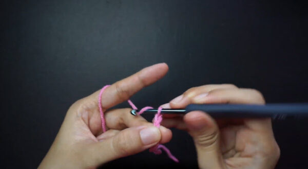 Hands starting a long foundation chain with pink yarn.