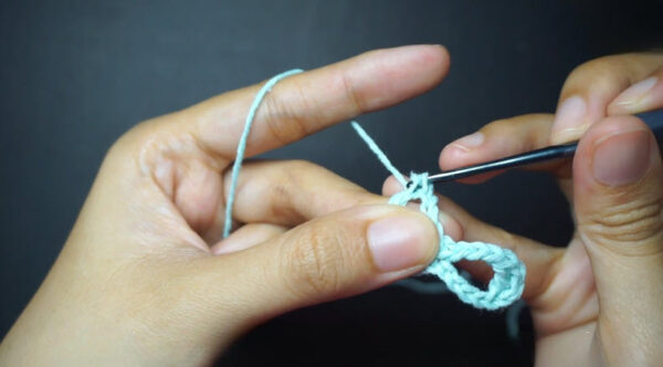 Hook chaining stitches with mint yarn in loose loop.
