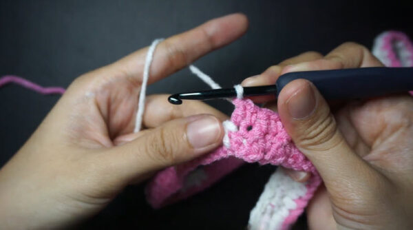 Hook crocheting checkered pattern with pink and white yarn.