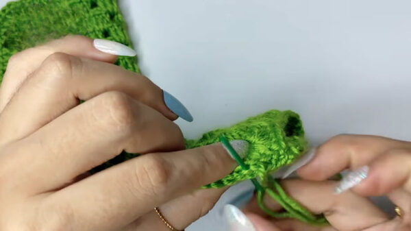 Hook joining a green crocheted piece into a small round shape.
