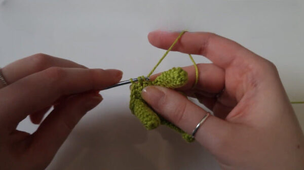 Hook joining crocheted legs onto a green dinosaur body