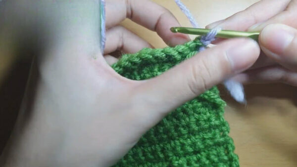 Lilac thread being pulled through the edge of a green panel.