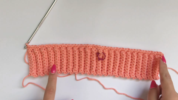 Peach ribbed crochet cuff with stitch marker attached.