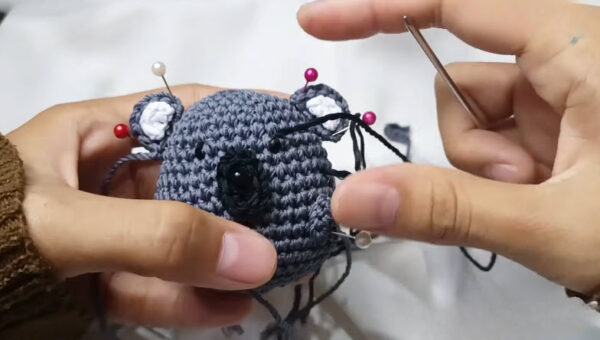 Pinned white ears and embroidered face on the gray koala amigurumi head.