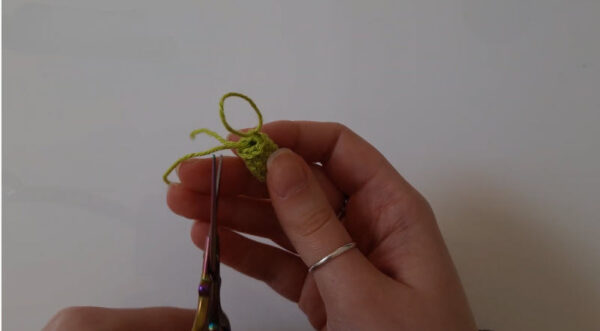 Scissors trimming loose threads on a green crochet piece.