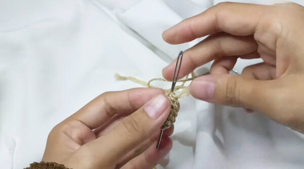 Sewing yarn tail into the tan crochet piece with a needle.
