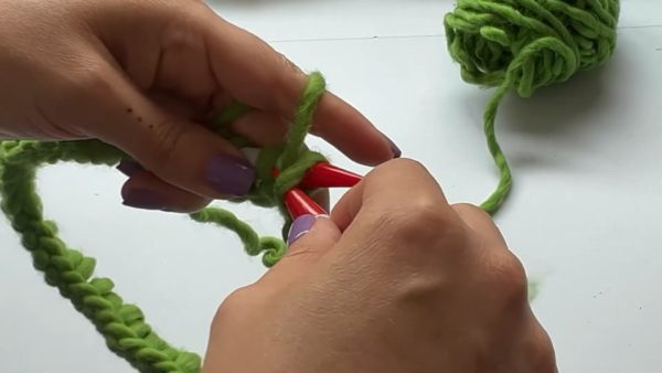 Casting on green chunky yarn with two red-tipped needles