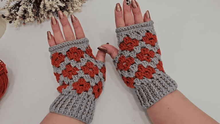Gray and rust orange crochet fingerless gloves with flower clusters and ribbed cuffs, shown on hands beside yarn