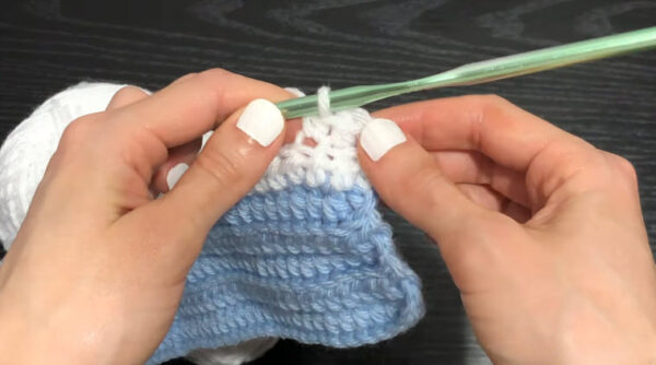 Crocheting white stripe stitches on the blue base of the sweater