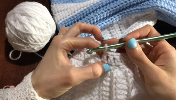 Crocheting a white ribbing border along the striped sweater edge