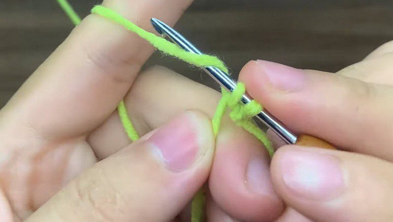 Fingers holding a steel hook and bright green yarn at the magic ring.