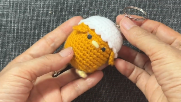 Finished crochet chick in a hat keychain wearing its white eggshell cap