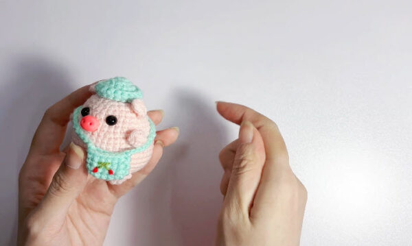 Finished student pig amigurumi: pink piglet wearing a mint hat and cherry apron