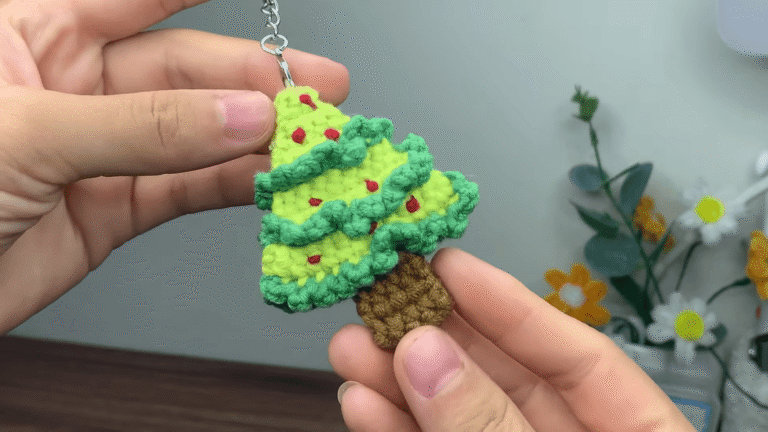 Green crochet Christmas tree keychain with ruffled tiers, red berry dots and a brown trunk, held in hand