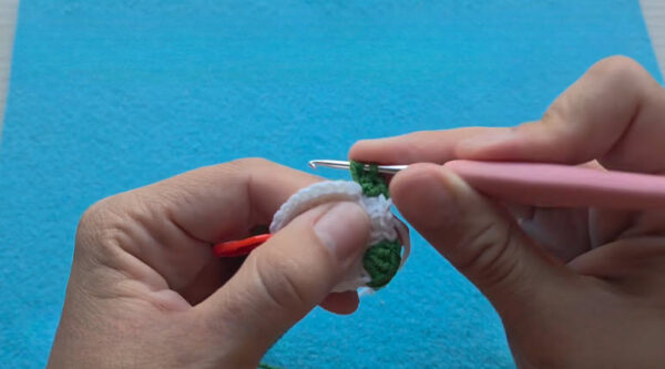 Green foot bobbles forming on the white stem of a crochet mushroom keychain