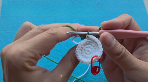 Green yarn joined to the white base for the feet of a crochet mushroom keychain