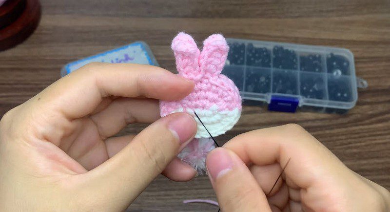 Needle stitching black thread onto a pink and white bunny head with ears.