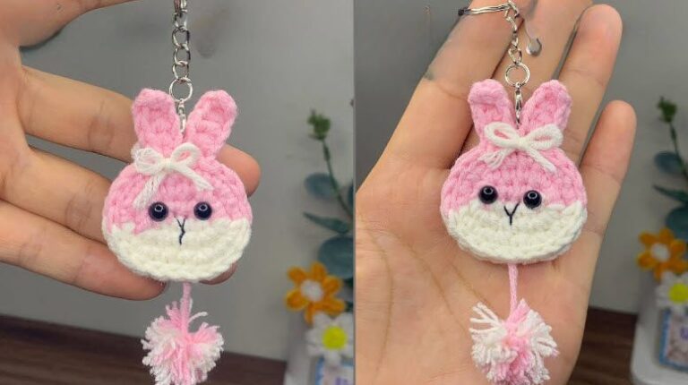 Pink and white crochet bunny keychain with a cream bow, black bead eyes and a fluffy pom pom tassel, held in hand