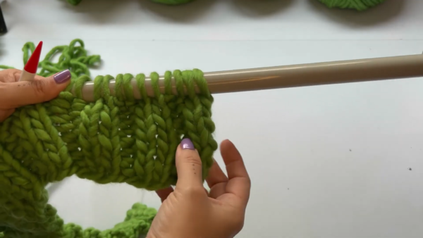 Green knitted panel with live stitches resting on a long needle