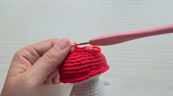 Red cap taking shape on the white body of a crochet mushroom keychain