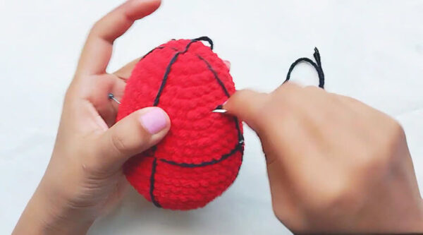Crochet Spider-Man keychain step: red piece with black yarn lines stitched across it