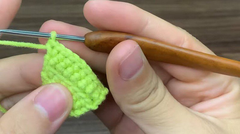 Small green triangle of tight stitches held beside a wooden handle hook.