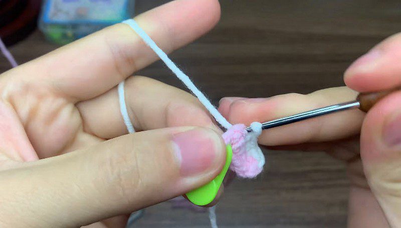 Small pink and white piece growing on the hook beside a green stitch marker.
