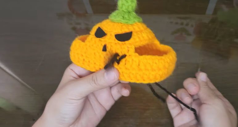 Stitching black eyes and zigzag mouth onto the pumpkin hat