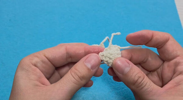 Tiny cream piece with loose yarn tails ready to shape.