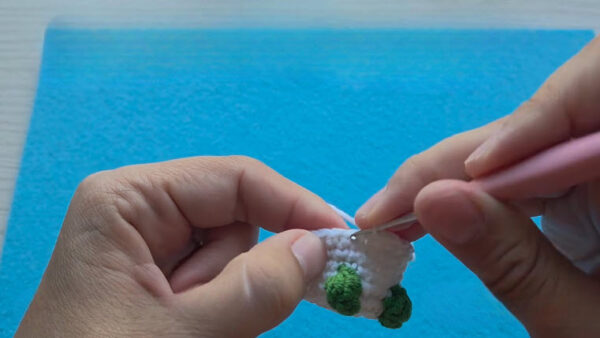 White body with two green bobbles added at the bottom of a crochet mushroom keychain