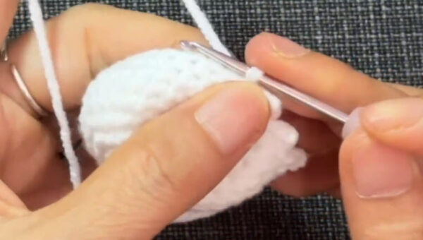 White yarn worked into the eggshell cap piece for the chick in a hat keychain